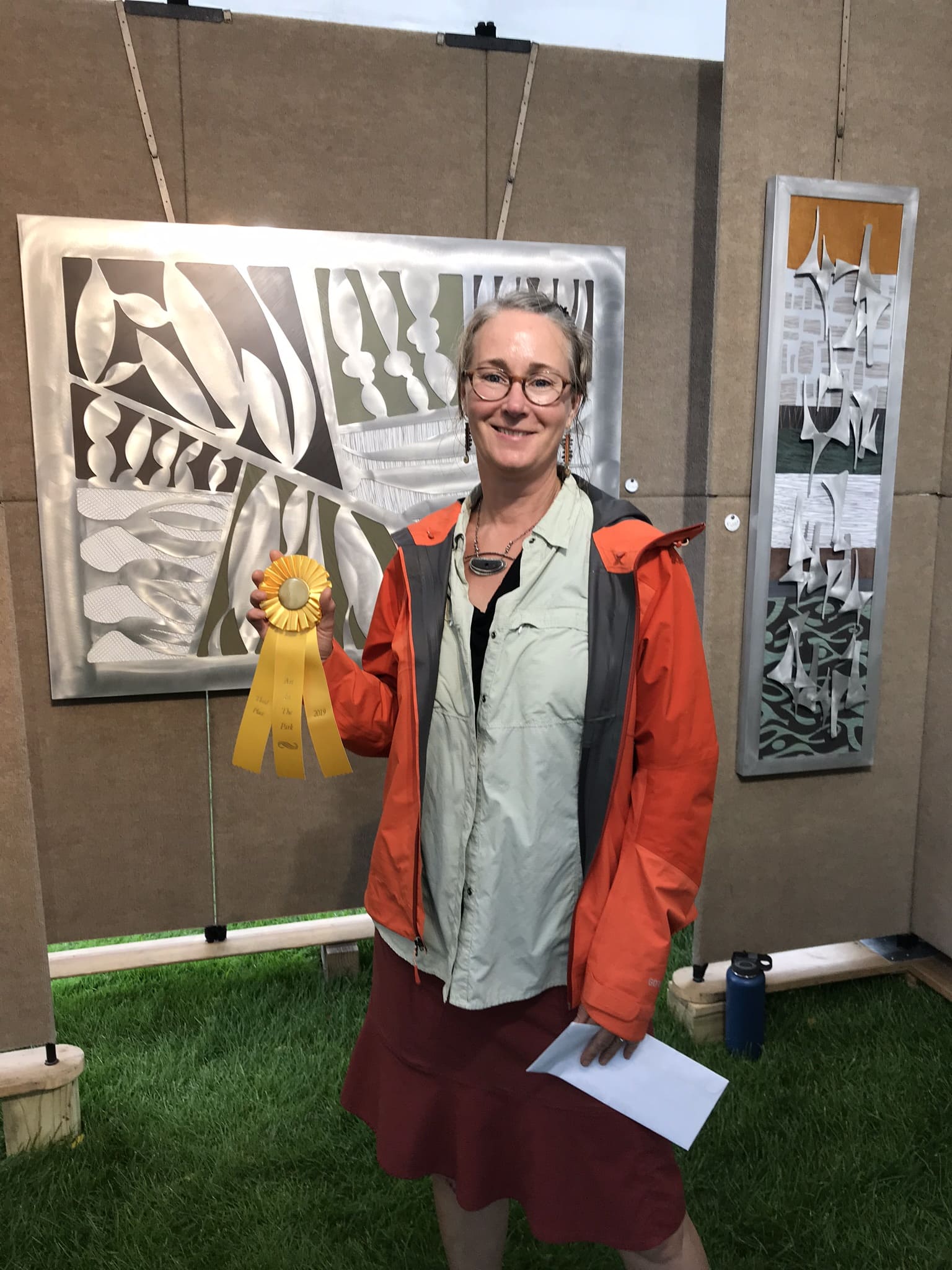 Cherie poses in front of her booth holding her award from the 2019 Petoskey art fair, Art in the Park.
