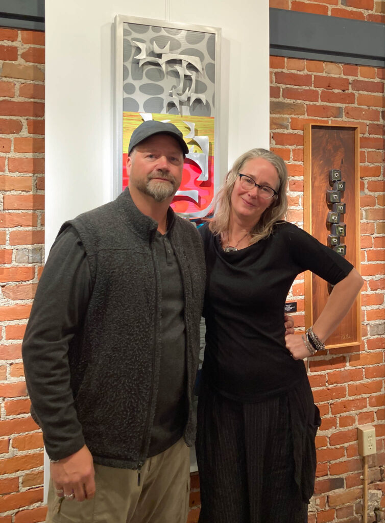 Chris Nordin and Cherie Haney posing in front of some of their artwork.